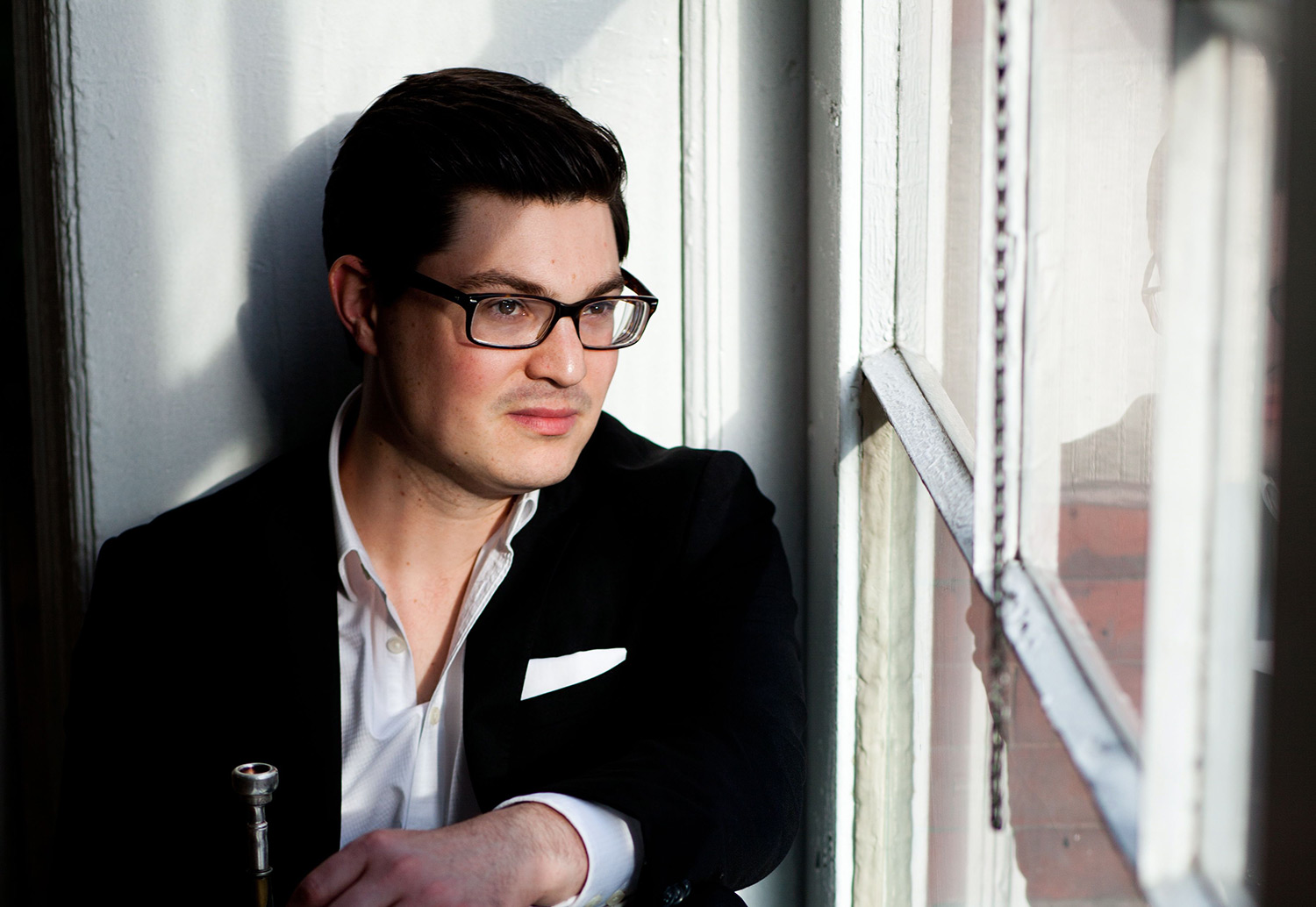 Tatum Greenblatt with trumpet, looking out a window