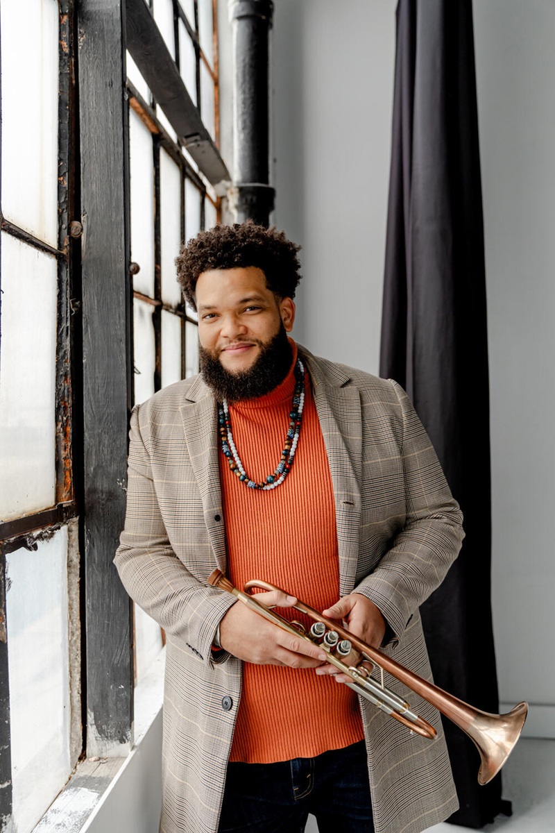 Kris Johnson leans against a window holding a trumpet