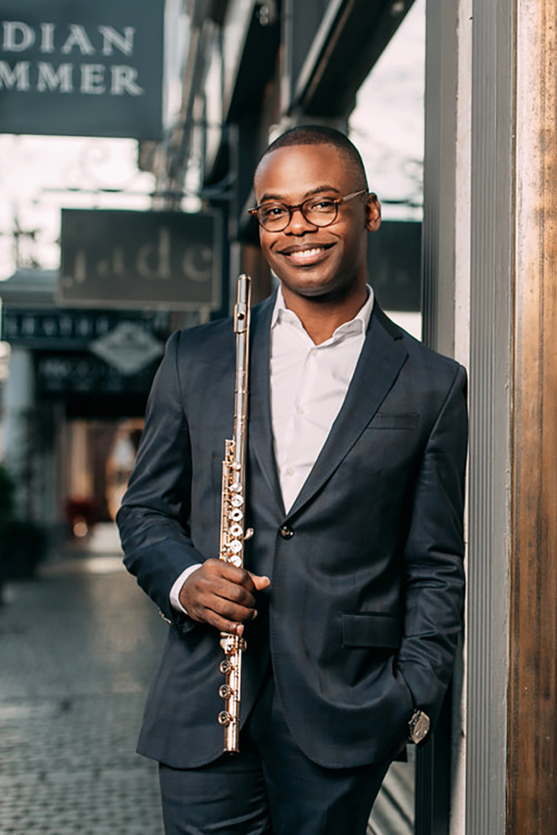 Demarre McGill standing on a brick sidewalk holding a flute